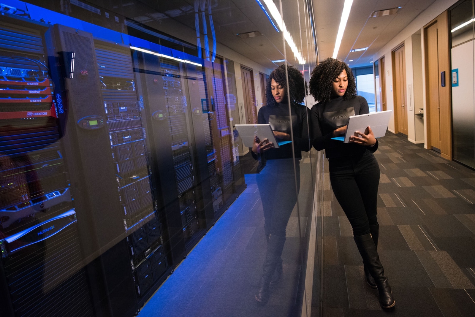 Engineer walking a lit server corridor with a laptop.